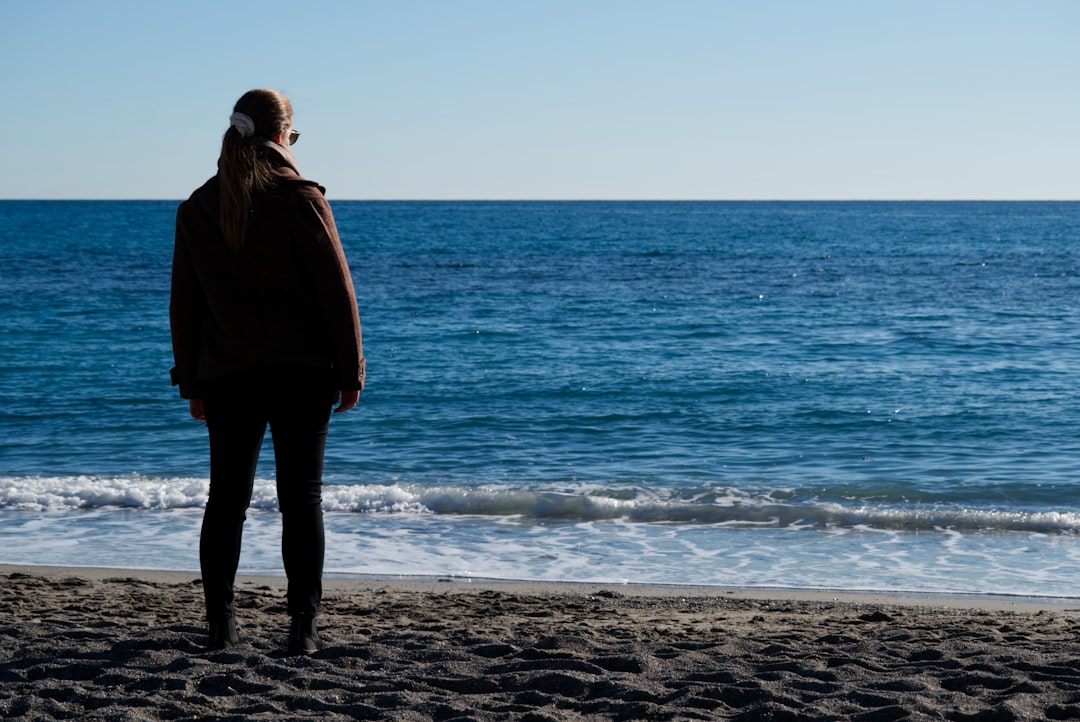 A woman standing on a quiet beach, embodying the calm and self-compassion cultivated through women's wellness hypnotherapy